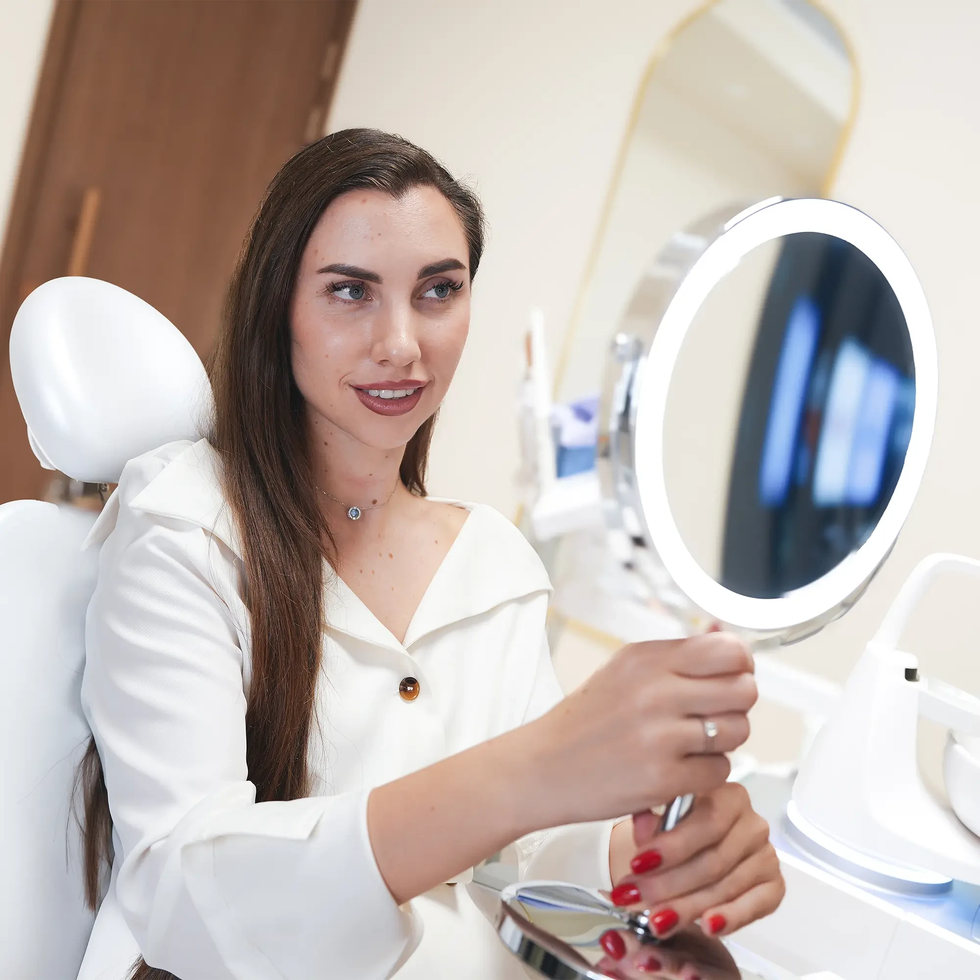 A girl with a beautiful smile and straight teeth looks in the mirror while sitting in the dentist's chair